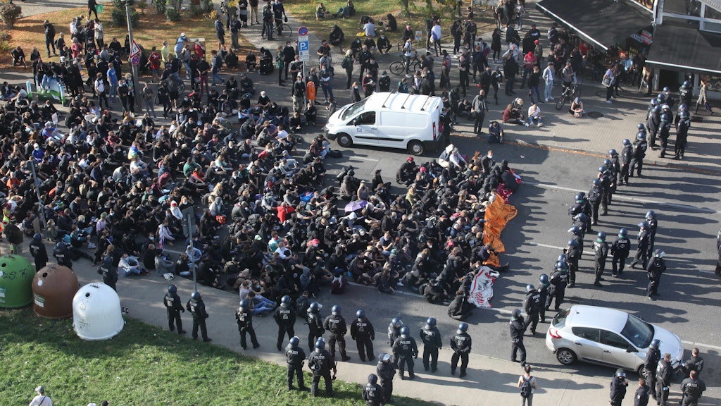 Polizisten haben die Sitzblockade der Gegendemonstranten umstellt. Beamte tragen die ersten Linken weg.