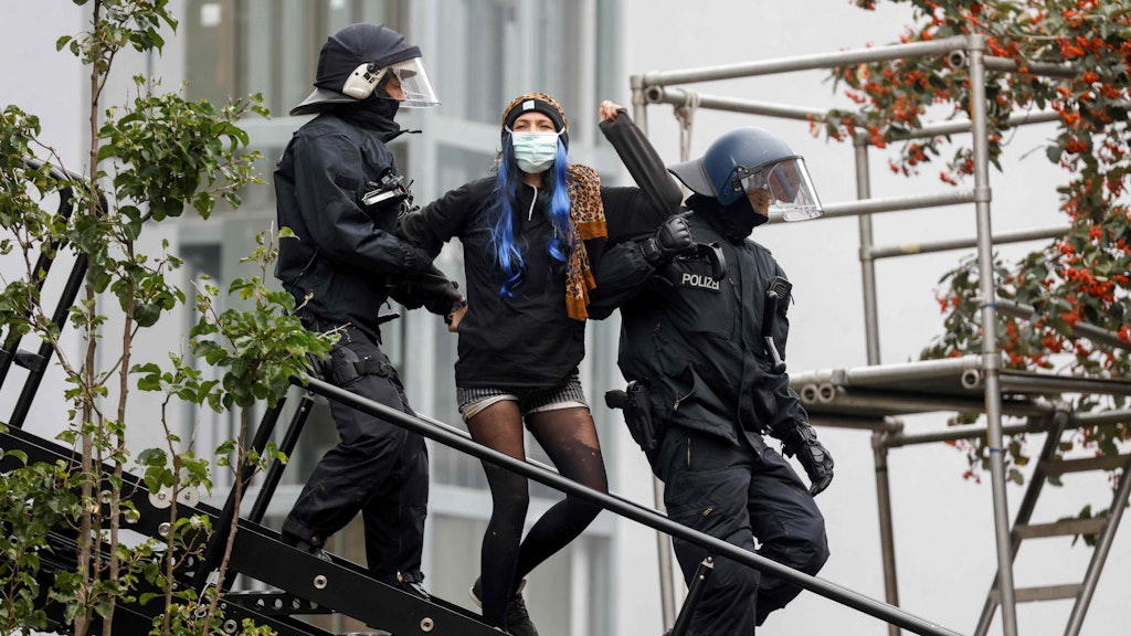 Eine Frau wird von Polizisten aus dem Haus geführt. 