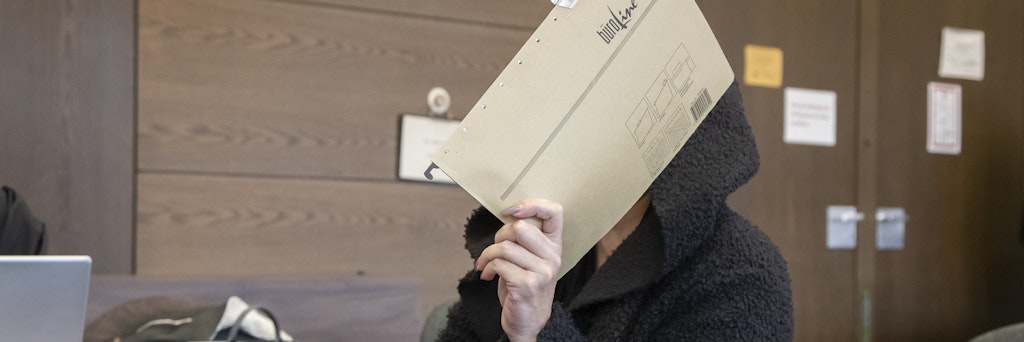 Die Angeklagte sitzt vor Gericht und verdeckt ihr Gesicht.