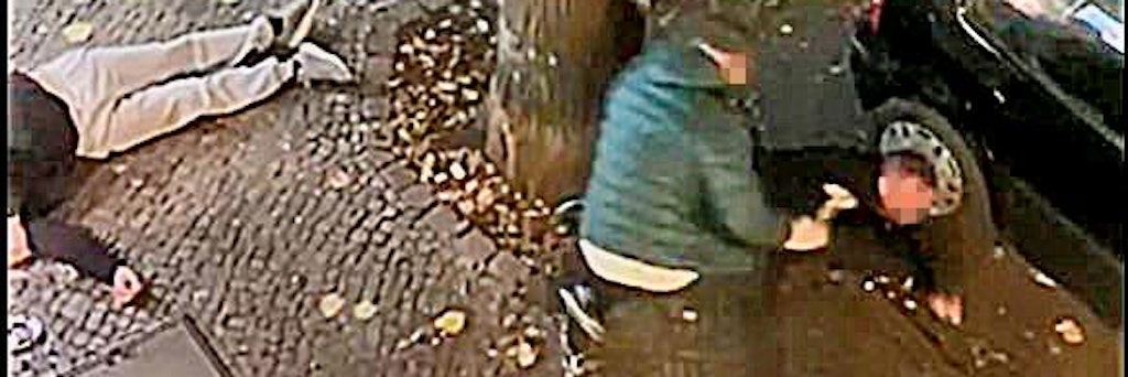 Zwei Männer liegen verletzt am Boden. Einer der Angreifer hat einen Hammer in der Hand.