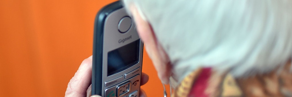 Eine Seniorin hält einen Telefonhörer an ihr Ohr.