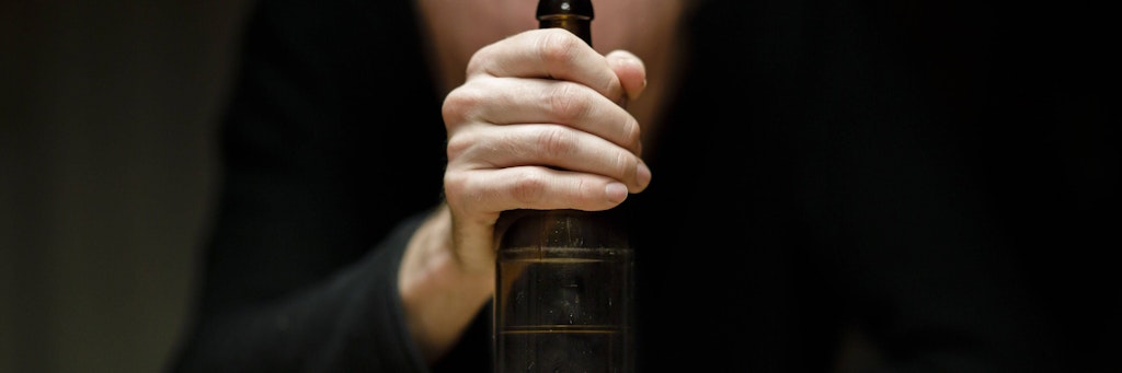 Ein Mann sitzt allein zu Hause an einem Tisch und hält eine Flasche Bier in der Hand. 
