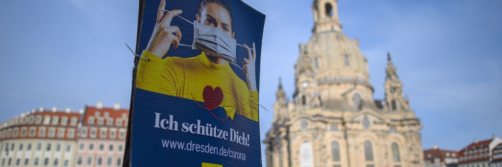 Ein Plakat weist vor der Dresdener Frauenkirche auf die Nutzung von Mund-Nasen-Masken hin. 