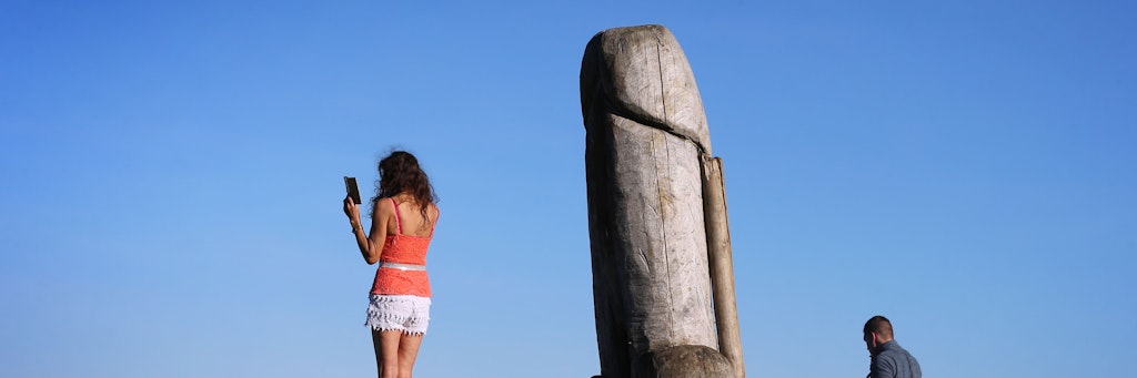 Eine Frau macht ein Selfie mit der zwei Meter hohen Penis-Skulptur aus Holz auf dem Grat des Grünten.