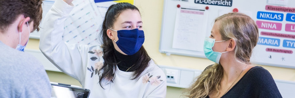 Schüler sitzen mit Mund-Nasen-Bedeckungen im Unterricht. 