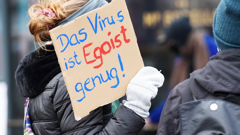 Eine Teilnehmerin der Gegendemonstration "Kritisch bleiben, Abstand halten, Freiheit solidarisch leben" gegen die Querdenken-Bewegung zeigt ein Schild mit der Aufschrift " Das Virus ist Egoist genug". 