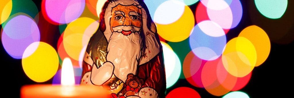 Ein Schoko-Weihnachtsmann steht vor einer brennenden Adventskerze. Im Zeitraum vom 23. Dezember bis 1. Januar können Treffen eines Haushaltes mit haushaltsfremden Familienmitgliedern oder haushaltsfremden Menschen bis maximal zehn Personen ermöglicht werden.