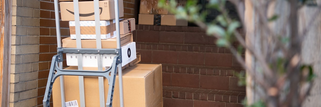 Pakete stehen auf einer Karre, während ein Paketzusteller Pakete ausliefert.