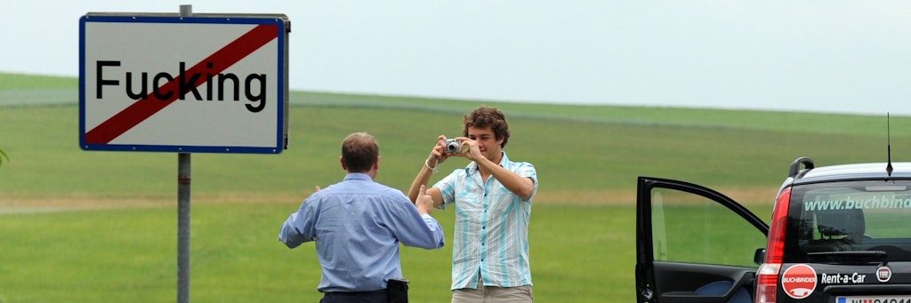 Touristen machen am Ortsschild von Fucking ein Foto.
