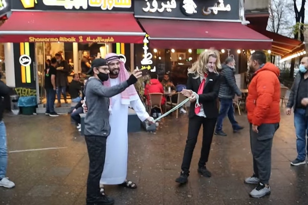 Fayez Kanfash führt einen Mann mit Macron-Maske durch Neukölln.