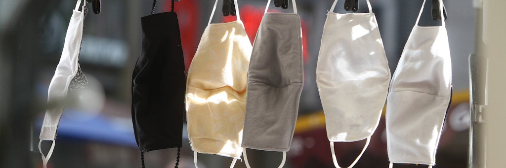 Modische Mund- Nasen Masken aus Biobaumwolle, hergestellt in handwerklicher Näharbeit, hängen an einem Marktstand.