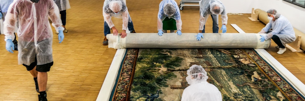 Mitarbeiter des Bayerischen Nationalmuseums rollen eine Tapisserie zusammen und verpacken sie vor der Übergabe an die Beauftragten der Erbengemeinschaft.