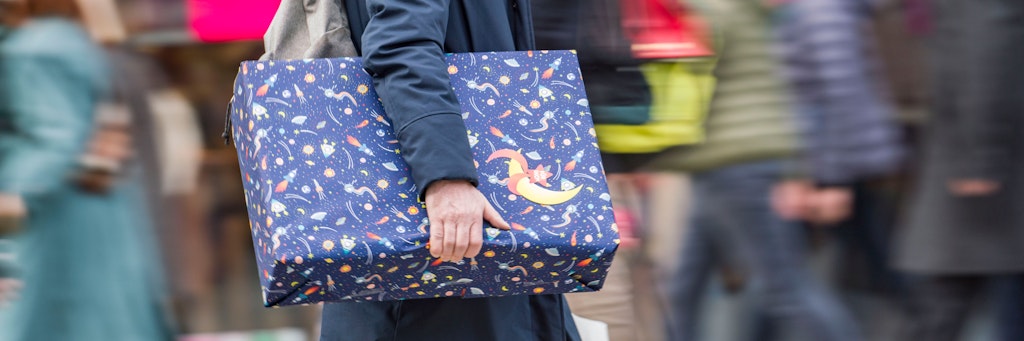 Ein Mann eilt mit einem verpackten Geschenk zwischen den anderen Passanten die Einkaufsmeile Zeil entlang.