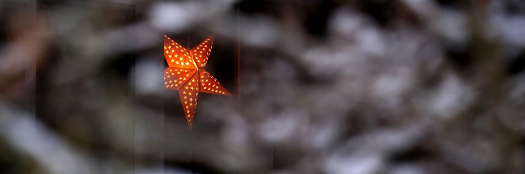 Eine Stern-Lampe hängt am Fenster eines Hauses hinter einem schneebedeckten Baum. Doch die Chancen auf weiße Weihnachten stehen schlecht.