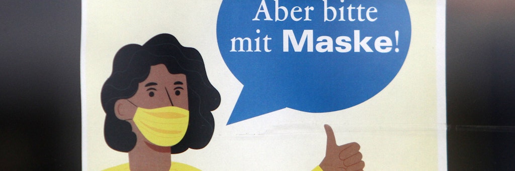 Schild mit Piktogramm und Aufschrift: „Aber bitte mit Maske!“, an der Tür eines Einzelhandelsgeschäftes.