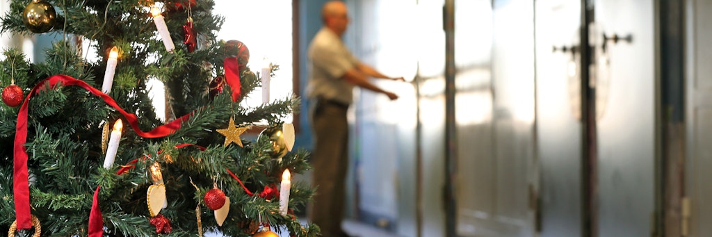 Auf einem weihnachtlich geschmückten Gefängnisflur schließt ein Justizvollzugsbeamter eine Zellentür ab.