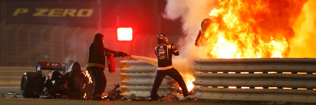 Romain Grosjean (r.) springt aus seinem brennenden Boliden, während Streckposten versuchen zu löschen.