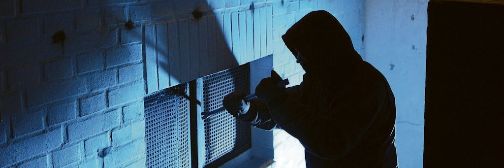 Ein Einbrecher macht sich bei einem Kellerfenster zu schaffen (Symbolfoto).