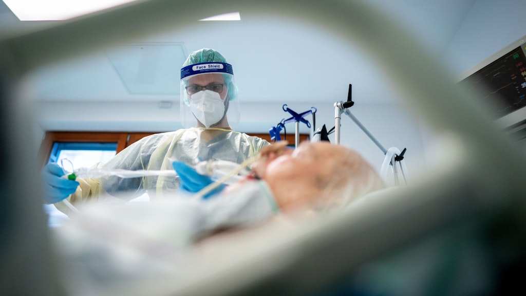 Intensivpfleger Sebastian arbeitet in Schutzausrüstung mit Mund-Nasenbedeckung, Gesichtsschutz, Kittel und Haube auf der Intensivstation des Krankenhauses Bethel Berlin an einem Corona-Patienten. Der Patient liegt im künstlichen Koma und wird beatmet. 