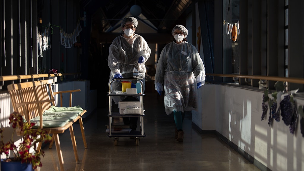 Zwei Altenpflegerinnen in Schutzausrüstung, die sie für die Durchführung von Antigen-Corona-Schnelltest angelegt haben.