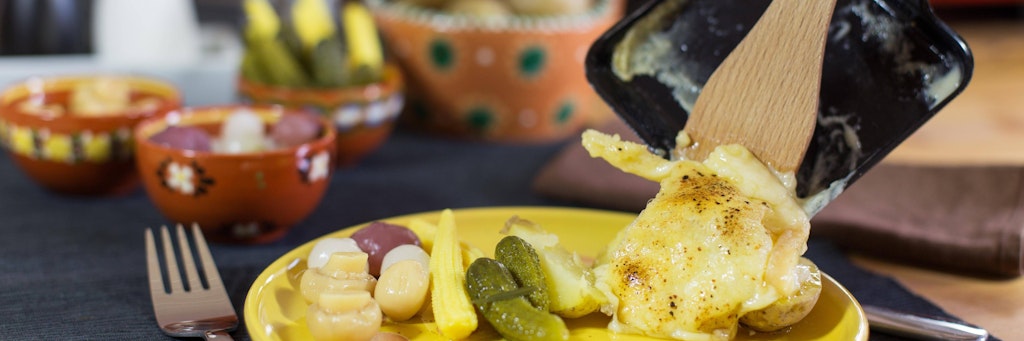 Klassisches Raclette mit eingelegtem Gemüse und Käse aus der Pfanne.