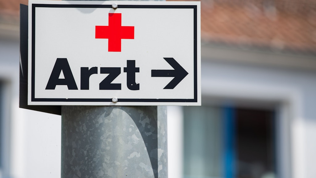 Ein Schild mit der Aufschrift „Arzt“ hängt an einer Straßenlaterne (Symbolfoto).