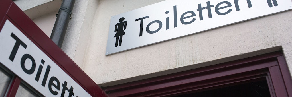 Hinweisschilder sind an der Tür zur öffentlichen Toilettenanlage zu sehen. Mehrfach schon wurde bei Corona-Studien Virenmaterial in menschlichen Ausscheidungen gefunden. 