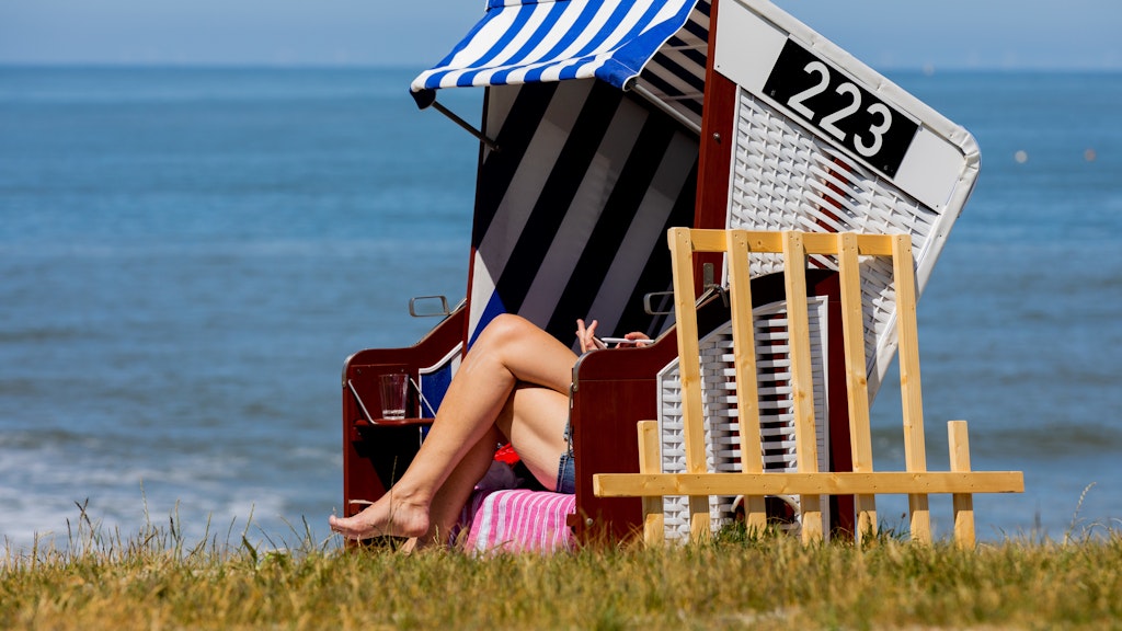 Eine Frau sonnt sich in ihrem Strandkorb am Meer.