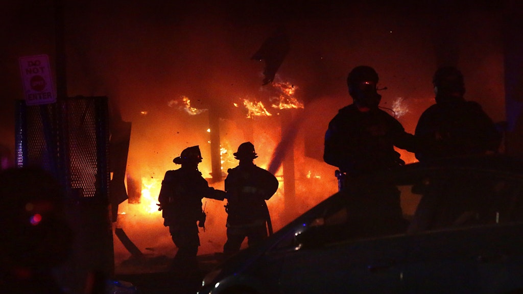 Geschützt von Polizisten, löschen Feuerwehrleute einen Brand im geplünderten 7-Eleven-Markt in St. Louis. 