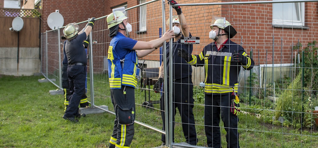In Verl stellen Feuerwehrleute Bauzäune auf. Ein ganzes Wohnviertel wurde dort unter Quarantäne gestellt.