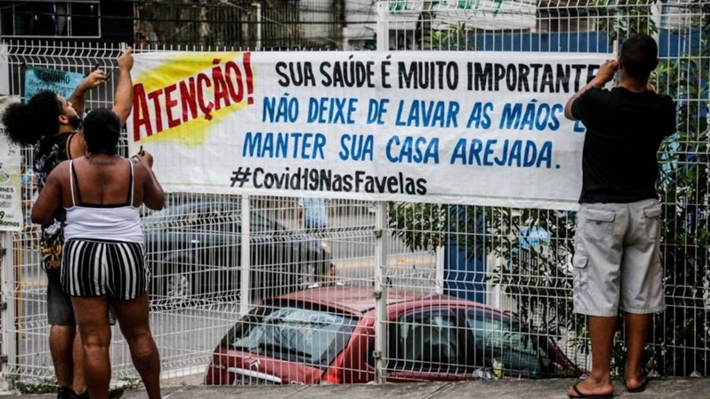 Bewohner der Favela Complexo do Alemão hängen ein Info-Plakat über das Coronavirus auf.