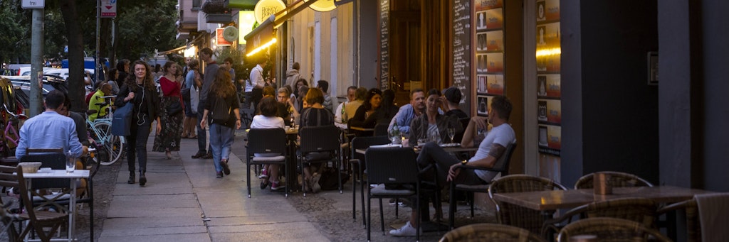 Besucher sitzen vor den Cafés und Kneipen entlang der Stargarder Straße.