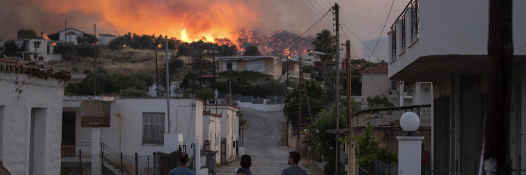 Drei Männer beobachten die Flammen eines Waldbrandes bei Korinth.