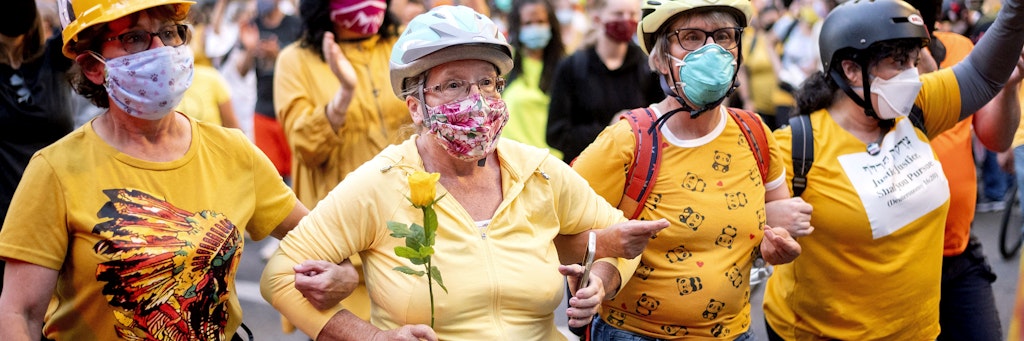 Norma Lewis hält eine Rose in der Hand, während sie sich mit ihren Mitstreiterinnen als menschliches Schutzschild gegen die Polizisten stellt.