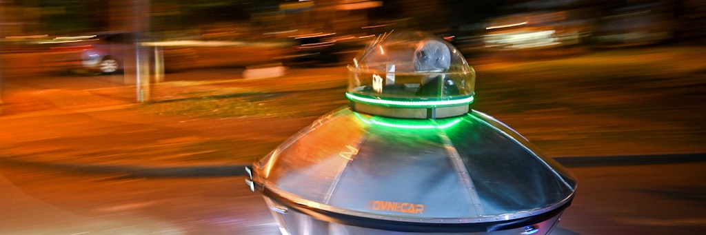 Ein Mann mit Alien-Maske sitzt in einem Gefährt, das aussieht wie ein Ufo.