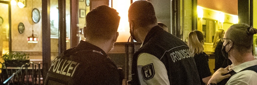 Ein Polizeibeamter und zwei Mitarbeiter des Ordnungsamtes stehen vor einem Lokal. Der Bezirksbürgermeister von Mitte, Stephan von Dassel (Grüne), will jetzt die Schließung von Fußballkneipen während der Champions League prüfen. 