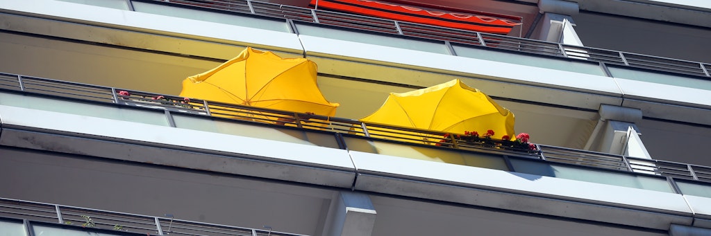 Mit Sonnenschirmen versuchen Bewohner eines Hochhauses in Mitte, sich vor der sengenden Hitze auf ihren Balkonen zu schützen.