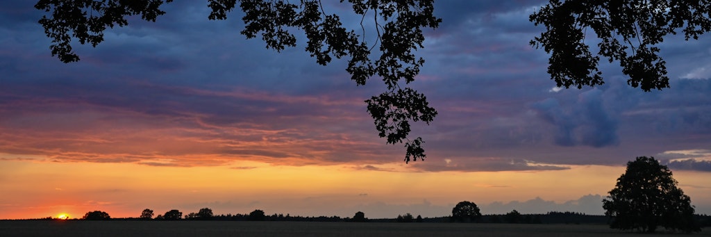 Farbenprächtig leuchtet der Sonnenuntergang zwischen der Brandenburger Landschaft und den dunklen Wolken am Himmel.