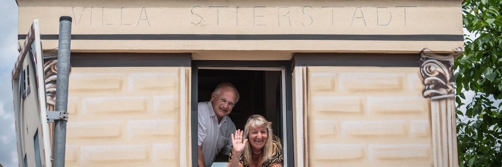 Achim Schollenberger und seine Partnerin Simone Stiefel winken aus dem ersten Stockwerk ihres winzigen Wohnhauses im Stadtteil Stierstadt.