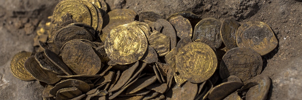 Goldmünzen liegen an einer archäologischen Ausgrabungsstätte, nachdem sie dort in einem Tongefäß ausgegraben wurden. 