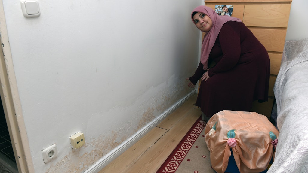 Hutiye A. zeigt, dass sie entlang der Scheuerleiste im Schlafzimmer den Schimmel beseitigt hat. Die Feuchtigkeit blieb, der Bodenbelag hebt sich.