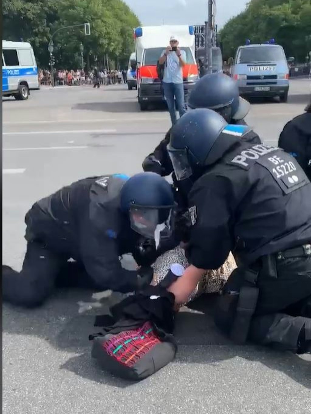 Einer der Beamten (links) schlägt mit der Faust in den Rücken der Frau.