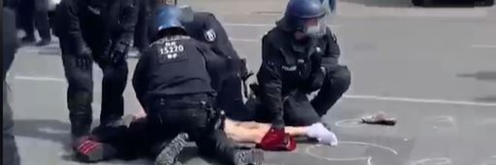 Vier Polizisten fixieren eine Demonstrantin. Das Vorgehen der Polizisten wirkt sehr rabiat. 