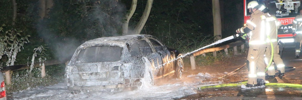 Feuerwehrleute löschen einen schwarzen Audi in Britz. Die Polizei geht davon aus, dass es sich dabei um den Fluchtwagen der Bankräuber handelt.