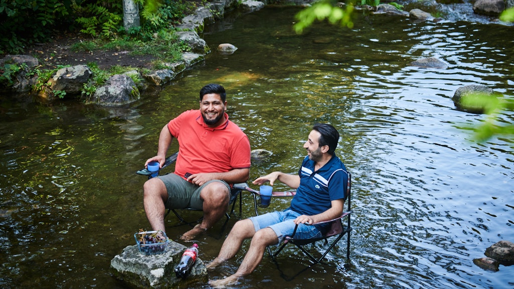Zwei Männer sitzen mit ihrem Campingstuhl am Wasserfall im Kreuzberger Viktoriapark. Der Sommer kommt mit viel Sonnenschein noch einmal zurück. 