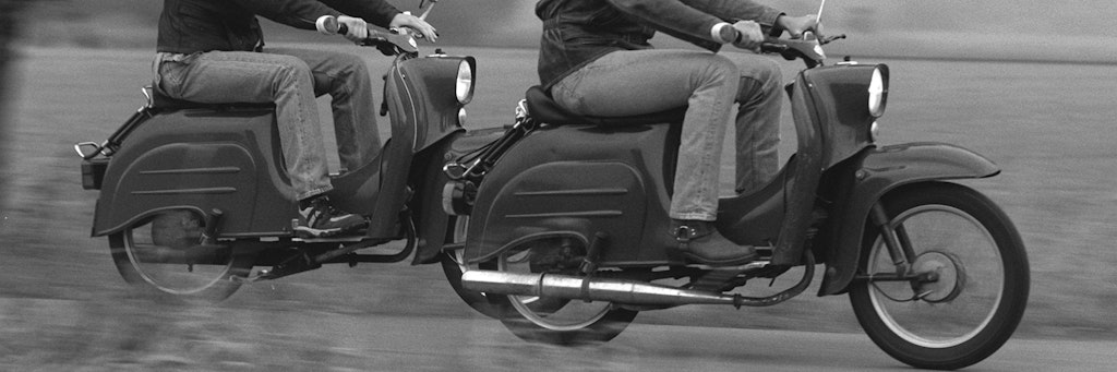 Zwei junge Männer fahren mit ihren „Schwalbe“-Rollern über einen Feldweg.