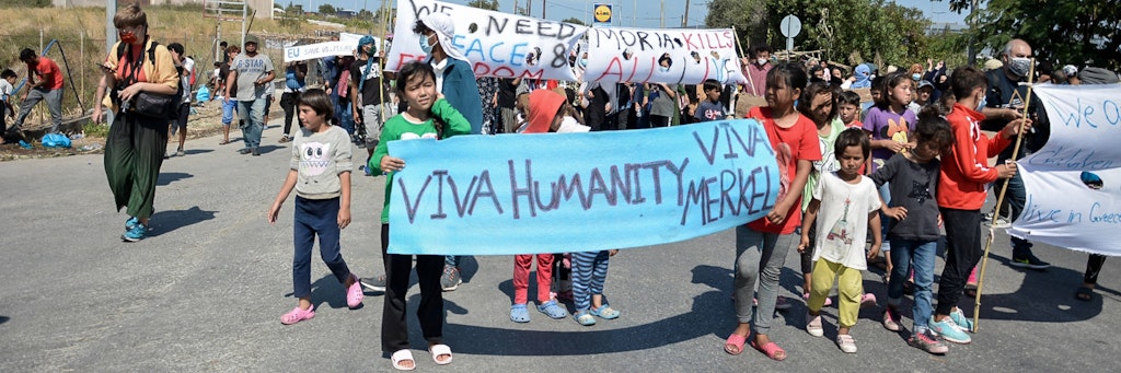 „Viva Merkel!“ Frauen und Kinder aus dem Flüchtlingscamp Moria demonstrieren mit Transparenten. Sie fordern Hilfe und wollen weg aus Griechenland.