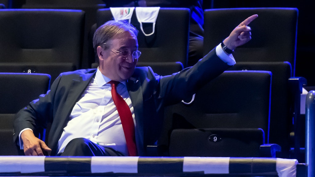 Gute-Laune-Verbreiter: Armin Laschet sitzt beim Festakt „75 Jahre NRW-CDU“ im Saal – und gestikuliert fröhlich.
