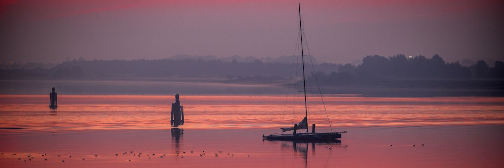 Schönes Meck-Pomm: Ein Segelboot liegt im rötlichen Morgenlicht in der Wismarbucht vor Anker.