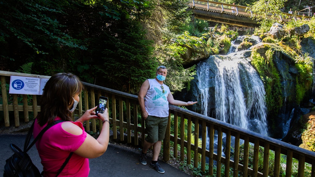Ein Tourist steht an einem Geländer und posiert für ein Foto an den Triberger Wasserfällen im Schwarzwald.